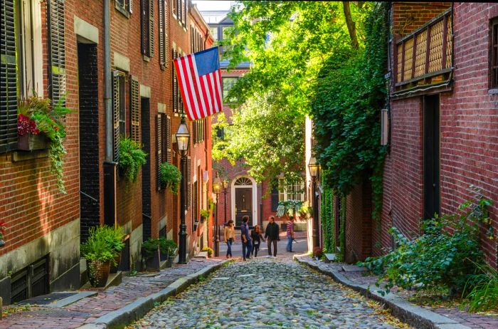 A narrow cobblestone street lined with historic buildings, one featuring a large American flag outside.