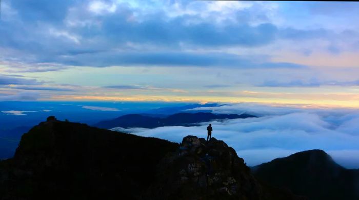 A solitary figure is silhouetted against the backdrop of a volcano as the sun begins to rise.