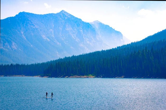 Paddle boarders glide across the Hyalite Reservoir on a sunny Montana day.