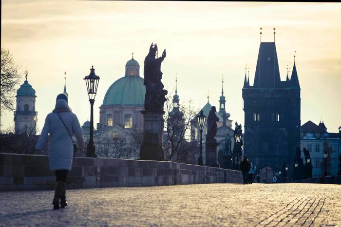 A lone individual strolls across a bridge adorned with large sculptures inspired by the human form on a winter day.