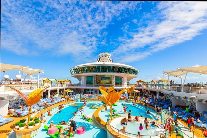 A view from the top of a Royal Caribbean cruise ship featuring a balcony overlooking a bustling pool area with guests and lounge chairs.