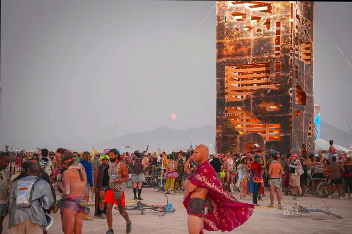 Colorfully dressed participants gather in front of a structure at the Burning Man festival, Black Rock Desert, Nevada, USA