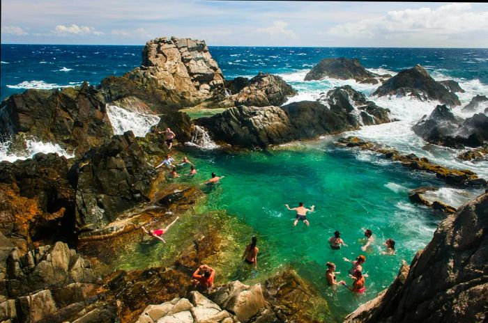 Tourists enjoying a swim in a secluded rock pool along Aruba's northern coast.