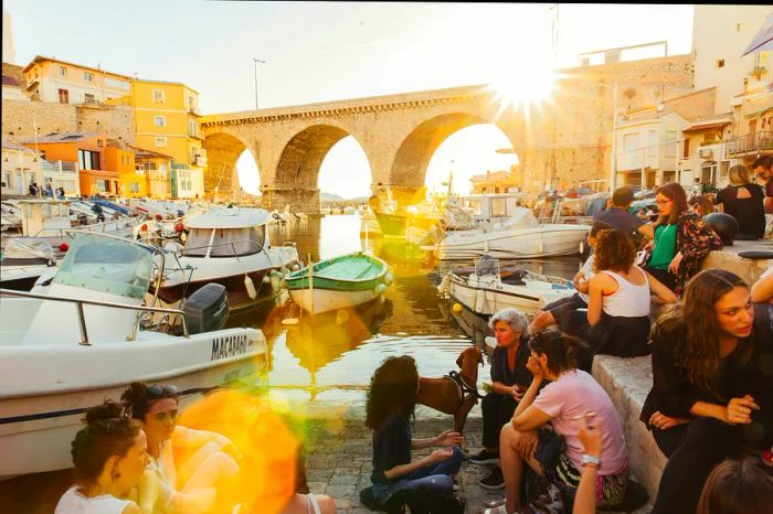 A group of people enjoying the sunset at Vallon des Auffes, a quaint fishing port in Marseille that once hosted many Italian and Spanish immigrants.