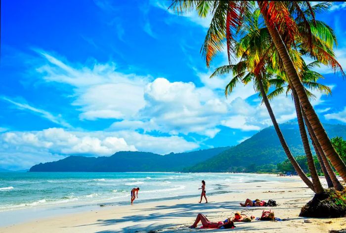 Visitors relax on the pristine white sands of Khem Beach beneath swaying palm trees.