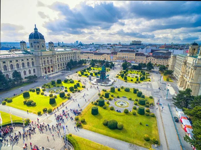 People stroll around a large square adorned with lawns and surrounded by museum buildings