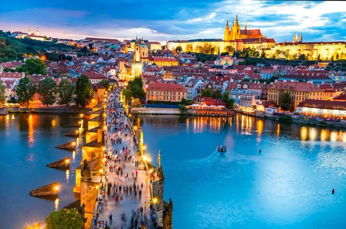 A view of Prague stretching across Charles Bridge, lined with statues, leading towards the castle atop the hill.