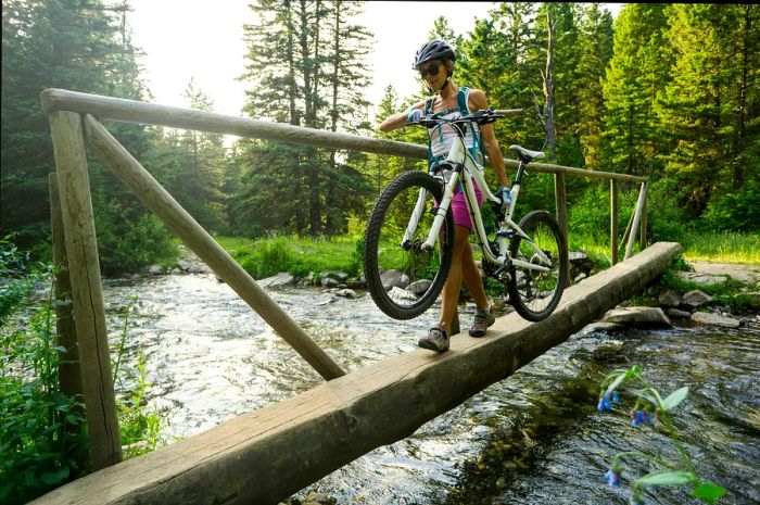 A woman carries her mountain bike across a wooden bridge near Bozeman, Montana