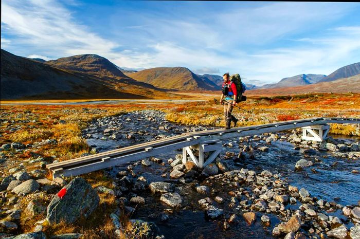 A long-distance hiker traverses an elevated section of the Kungsleden hiking trail across rocky terrain in Lapland.