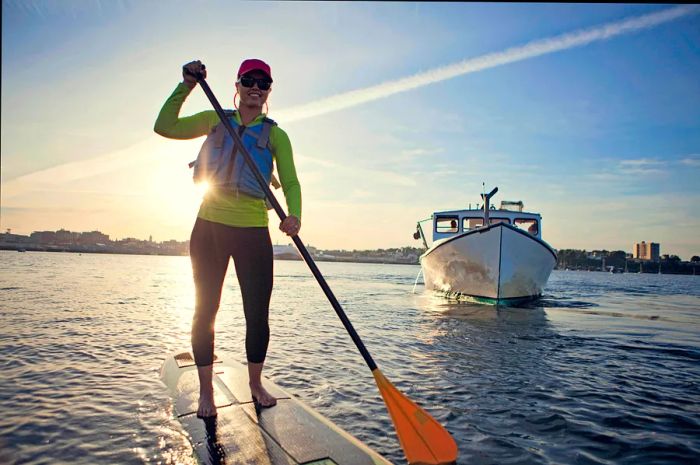 A cheerful young woman paddleboarding across the harbor in Portland, Maine, USA