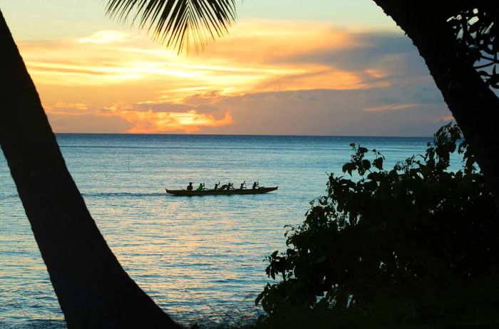 An outrigger canoe glides across the ocean at sunrise in Kihei, Maui