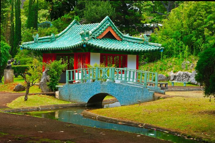 A red and teal temple with a bridge nestled amidst the lush greenery of Kepaniwai Park in Maui