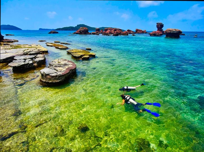 Two divers explore the vibrant underwater landscape around rocks in the clear waters of Hom Gam Ghi in Phu Quoc.