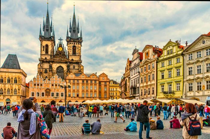 Tourists congregate in a city square beneath twin Gothic church spires