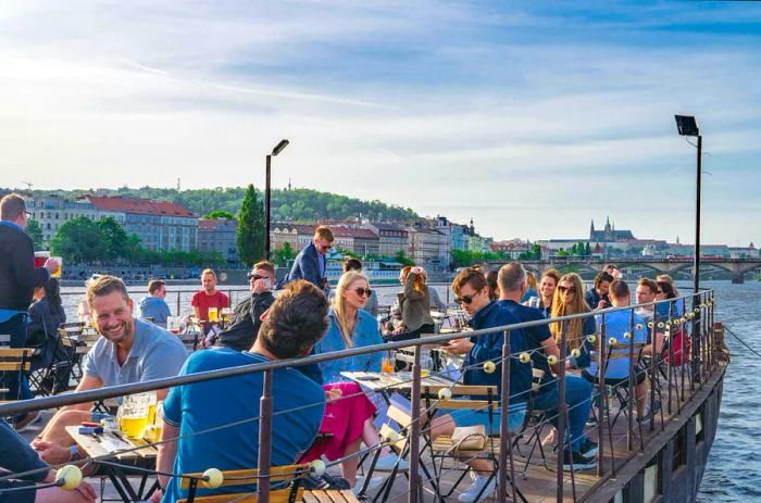 People basking in the summer sun at a riverside bar in Prague