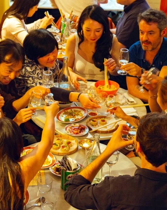 A group of friends at a table filled with diverse Asian dishes, raising their glasses