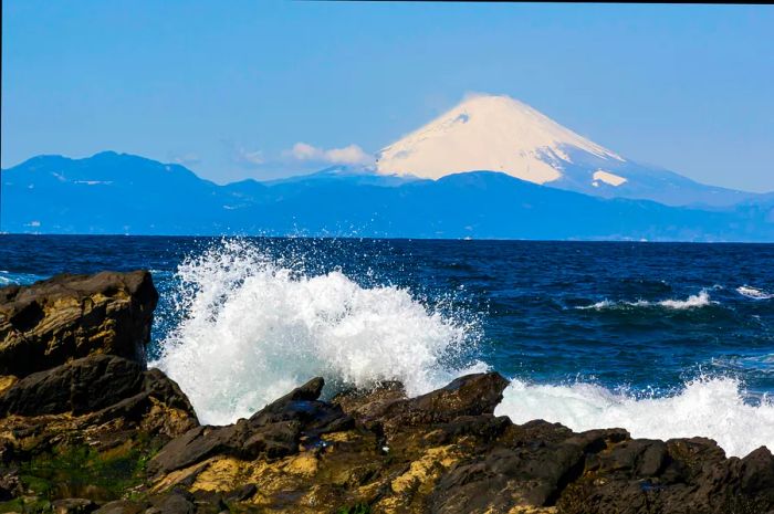 Waves crash against Shonan Beach, framed by the snow-capped peak of Mt Fuji in the distance, Misaki, Jogashima, Kanagawa, Japan