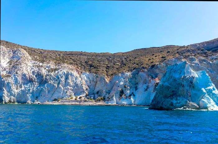 A view from the sea toward striking white chalk cliffs with a small beach nestled at their base.