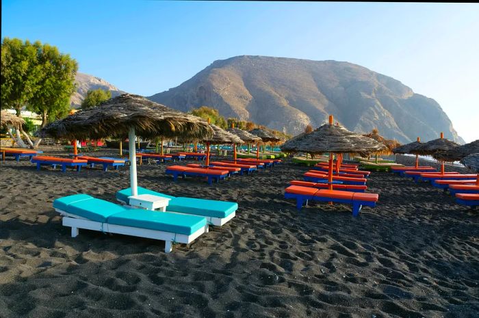 Empty tanning beds and umbrellas bask under the sun on a black-sand beach.