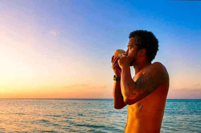 A man plays a traditional conch shell as the sun sets in Fiji, South Pacific