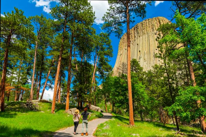 Two hikers gaze up at the towering rock formation known as Devils Tower in Wyoming, United States