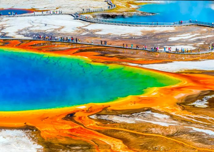 Visitors stroll along boardwalks surrounding vibrant geothermal lakes.