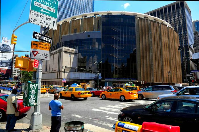 The facade of a large entertainment venue featuring a curved design, with numerous yellow taxis passing by.