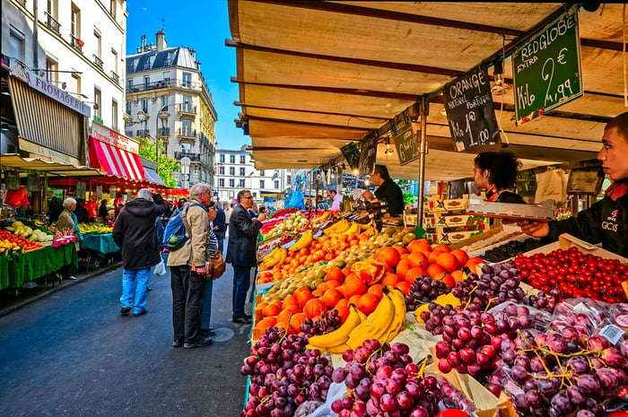 Shoppers gather at an outdoor market in France to select fresh produce.