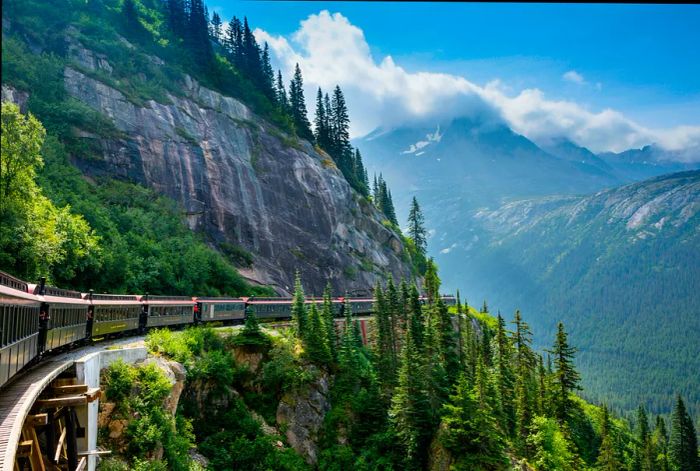 A heritage train winds along the cliffside in a mountainous region.