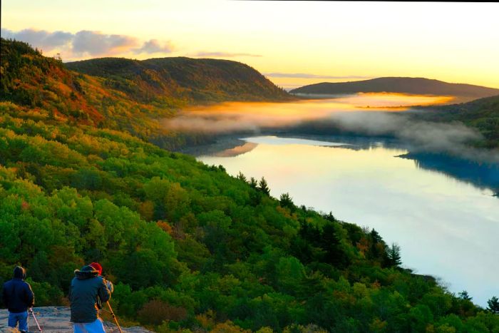 Two photographers capture the early morning mist rising over a lake surrounded by woods.