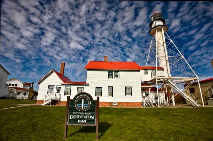 A lighthouse accompanied by red-roofed buildings. A sign reads