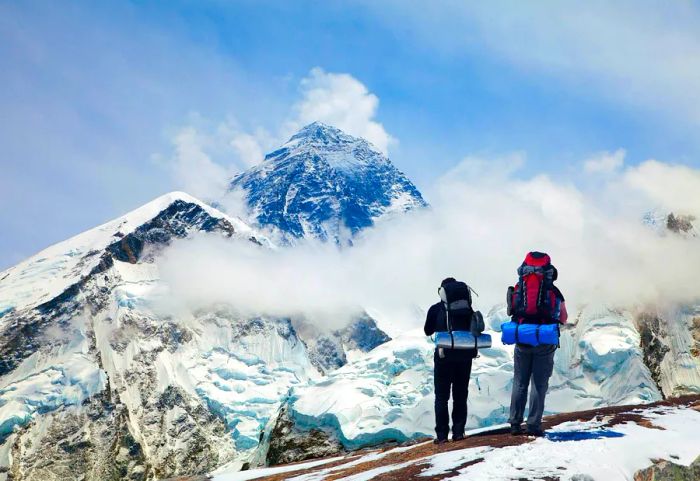 Snow-capped Mount Everest viewed from Kala Patthar, with two trekkers carrying large backpacks