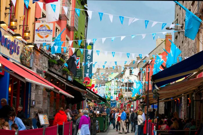 People strolling down Shop Street, surrounded by colorful shops and festive bunting, in Galway during the daytime.