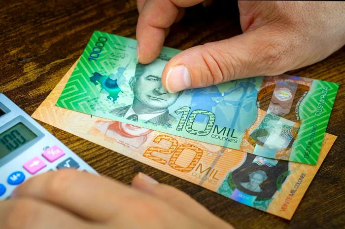 A man calculating expenses while holding Costa Rican currency