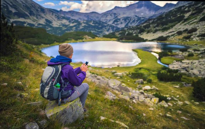 Traveler using a smartphone while sitting by a lake in the Pirin Mountains, Bulgaria