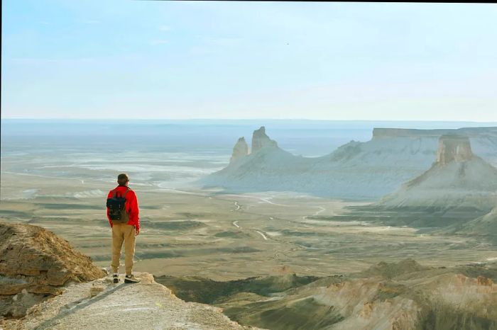 A hiker gazes out over the Boszhira mountains from a mountain peak in the Ustyurt Plateau, Kazakhstan