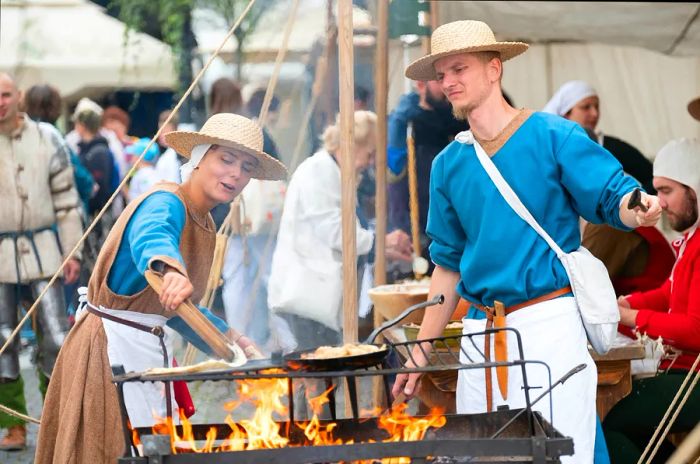 At a festival in Zilina, Slovakia, a man and woman in traditional attire grill flatbread.