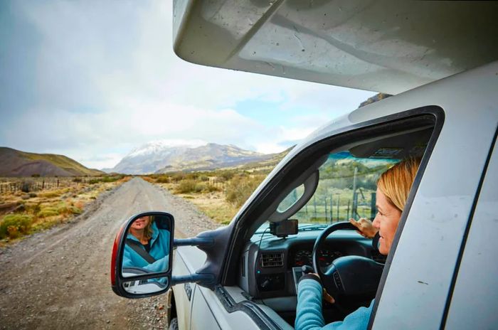 A woman gazes out of a campervan window, taking in the stunning mountainous landscape.