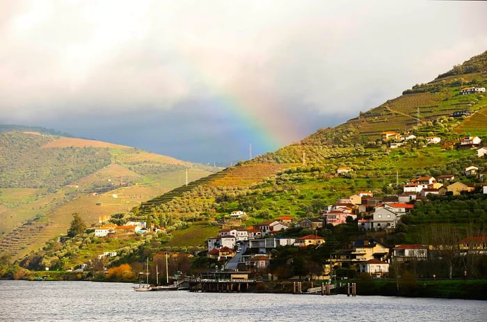 A rainbow arches over a riverside village and vineyards