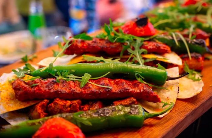 A wooden platter featuring a Turkish mixed grill with meat and green peppers