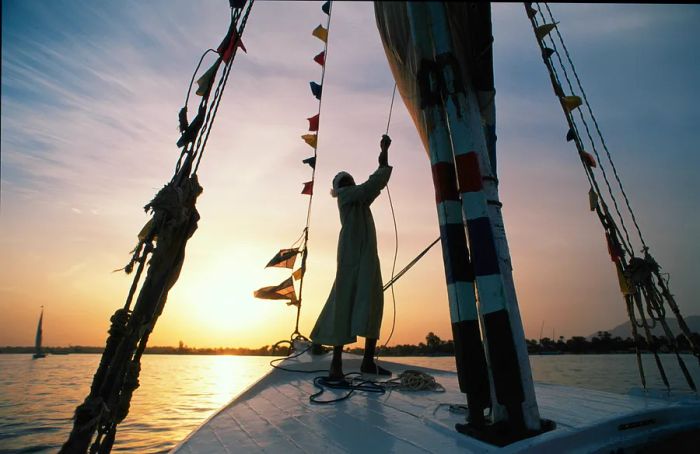 A man sails a felucca on the Nile River at sunset in Aswan, Egypt