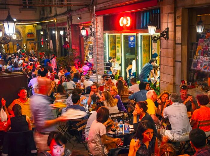 A bustling outdoor seating area of a bar in the Beyoğlu district of Istanbul is filled with patrons.