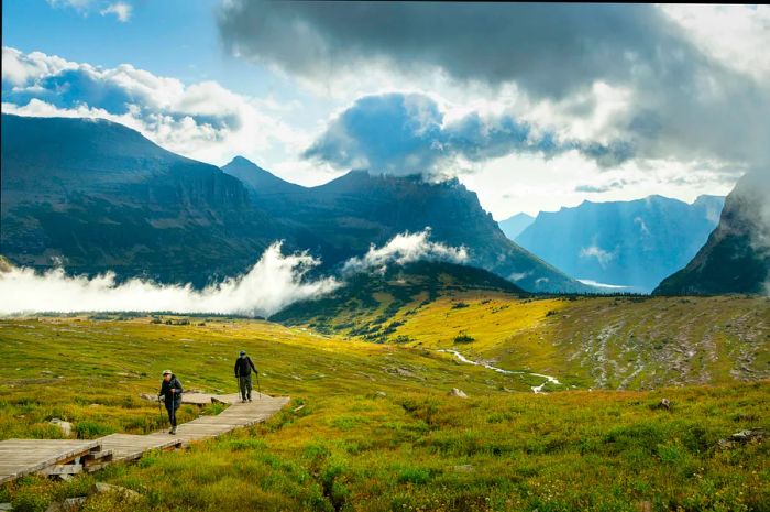 Visitors stroll along a trail in Glacier National Park, framed by mountain peaks shrouded in clouds.