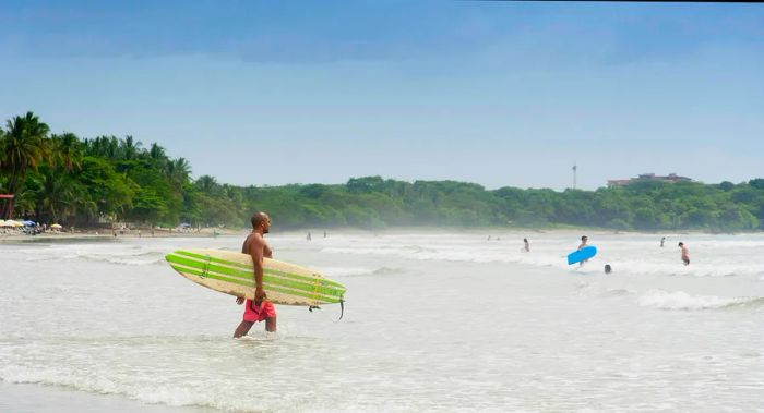 A man carrying his surfboard into the ocean at Tamarindo beach in Costa Rica.