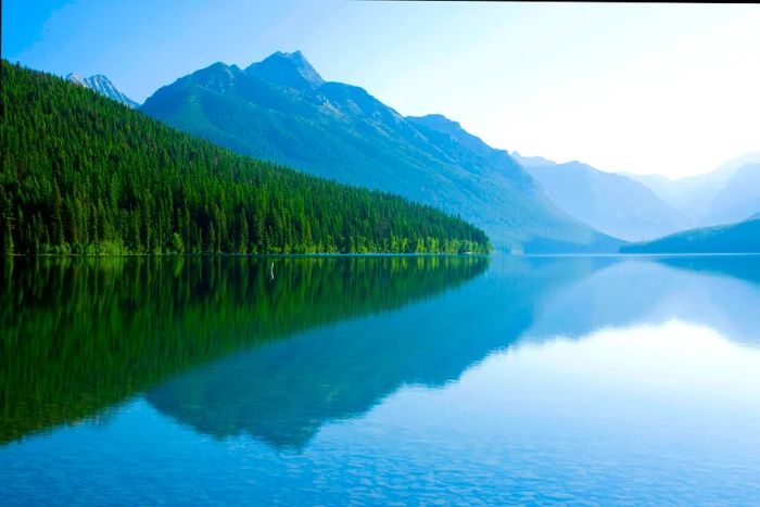 Stunning mountains mirrored in the calm, crystal-clear waters of Bowman Lake in Glacier National Park.