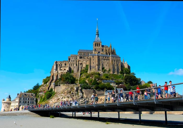 Individuals walking along a path across the bay towards Mont St-Michel, Normandy, France