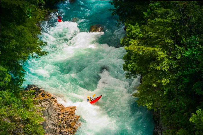 A rafter navigates through the turbulent white water rapids of a wide river