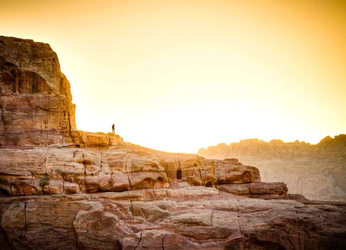 A solitary hiker perched on a rock in Petra, Jordan at sunset.