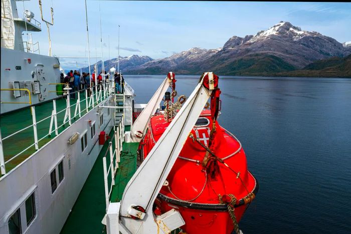 A cruise ship gliding through fjords, with passengers at the front taking in the breathtaking views.