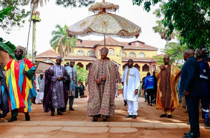 The Sultan King of the Bamouns presides over a ceremony in front of a palace, surrounded by numerous attendees.